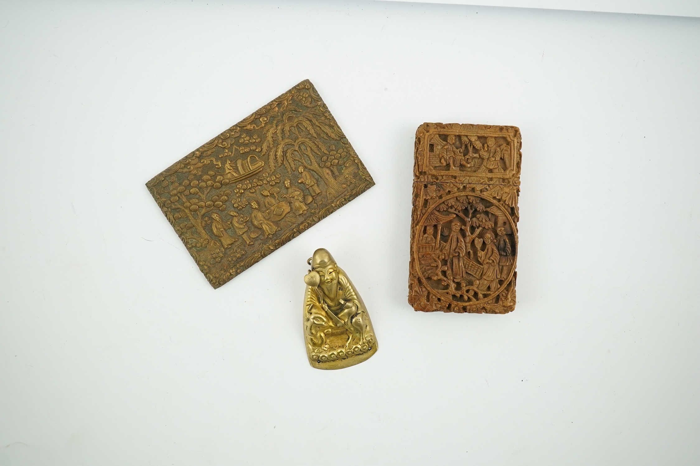 A Chinese carved sandalwood card case, a bronze relief cast and chased plaque and a gilt metal Shou Lao pendant, card case 7.5cm high. Condition - good